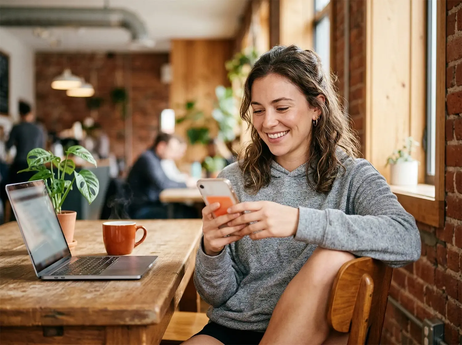 Young entrepreneur in a bright co-working space checking her phone with a pleased expression, burnt-orange coffee mug beside her